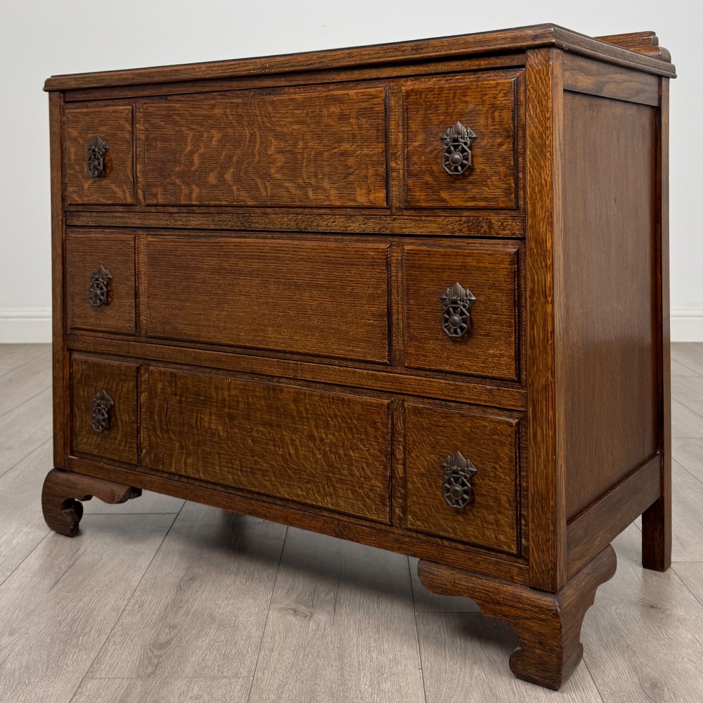 A twentieth-century dark oak chest of drawers featuring three drawers with geometric panel moulding, decorative drop handles, and shaped bracket feet. View II