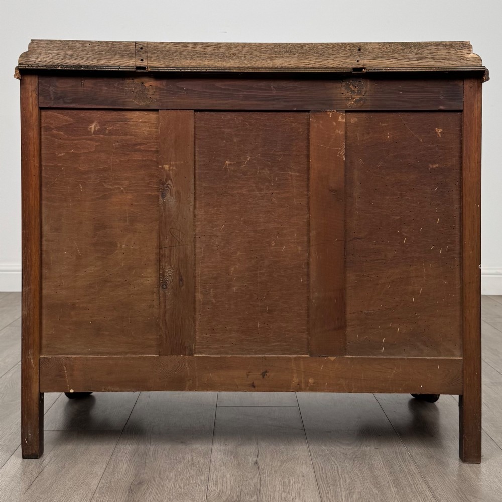 A twentieth-century dark oak chest of drawers featuring three drawers with geometric panel moulding, decorative drop handles, and shaped bracket feet. View V