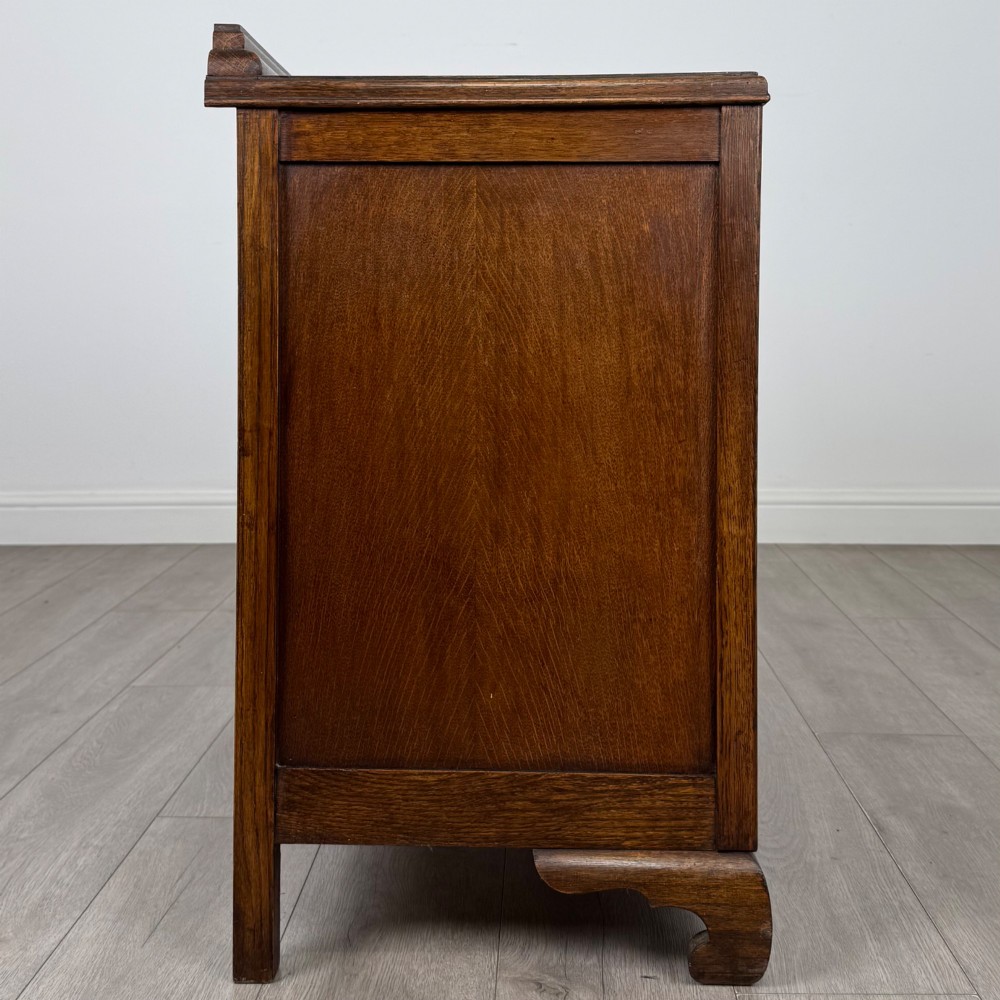 A twentieth-century dark oak chest of drawers featuring three drawers with geometric panel moulding, decorative drop handles, and shaped bracket feet. View VII