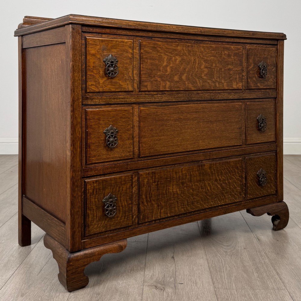 A twentieth-century dark oak chest of drawers featuring three drawers with geometric panel moulding, decorative drop handles, and shaped bracket feet. View VIII