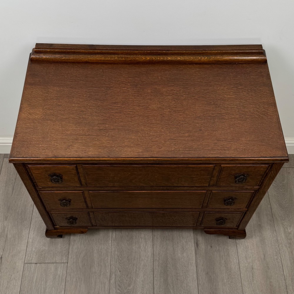 A twentieth-century dark oak chest of drawers featuring three drawers with geometric panel moulding, decorative drop handles, and shaped bracket feet. View IX