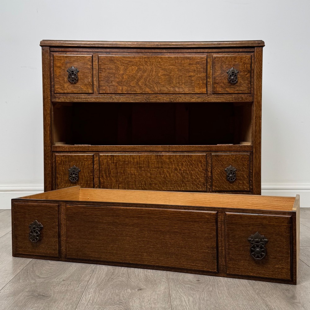 A twentieth-century dark oak chest of drawers featuring three drawers with geometric panel moulding, decorative drop handles, and shaped bracket feet. View X