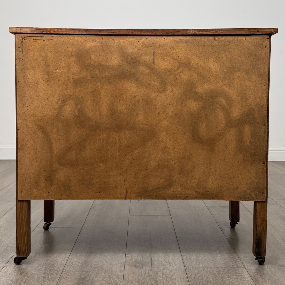 An early 20th-century golden oak side cabinet featuring a top drawer with ornate metal drop handles above a central panelled cupboard door on square legs with castors. View VI
