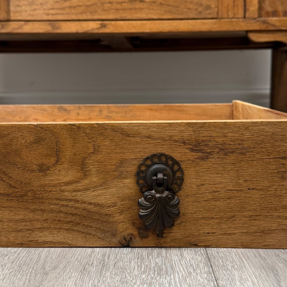 An early 20th-century golden oak side cabinet featuring a top drawer with ornate metal drop handles above a central panelled cupboard door on square legs with castors. View XII