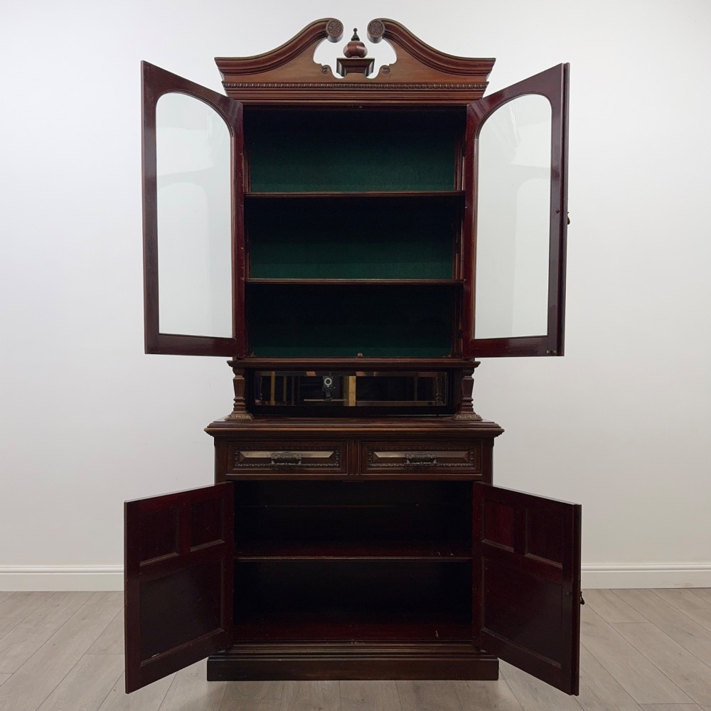A nineteenth-century dark mahogany glazed bookcase featuring a carved swan neck pediment, twin arched glass upper doors, and a lower two-door cabinet with carved panels. View II