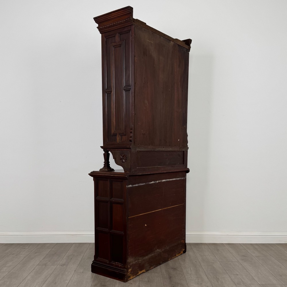 A nineteenth-century dark mahogany glazed bookcase featuring a carved swan neck pediment, twin arched glass upper doors, and a lower two-door cabinet with carved panels. View V