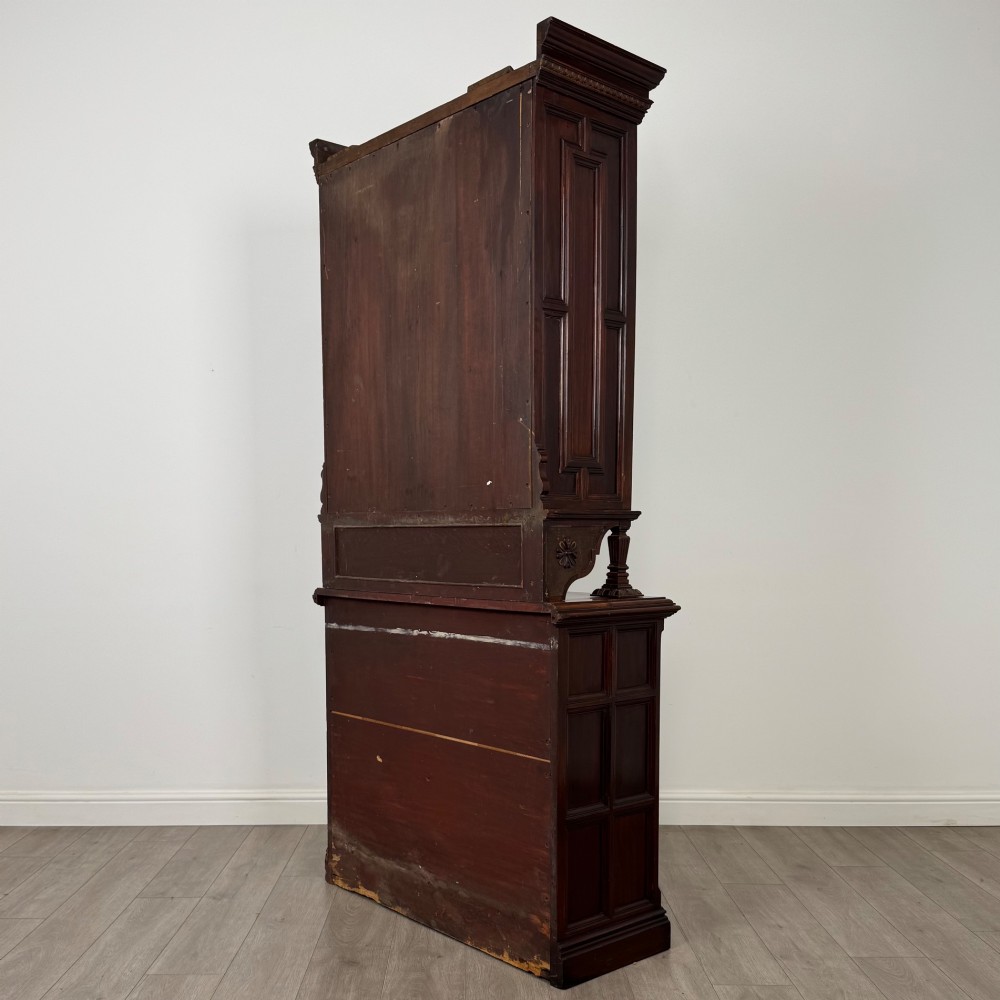 A nineteenth-century dark mahogany glazed bookcase featuring a carved swan neck pediment, twin arched glass upper doors, and a lower two-door cabinet with carved panels. View VII