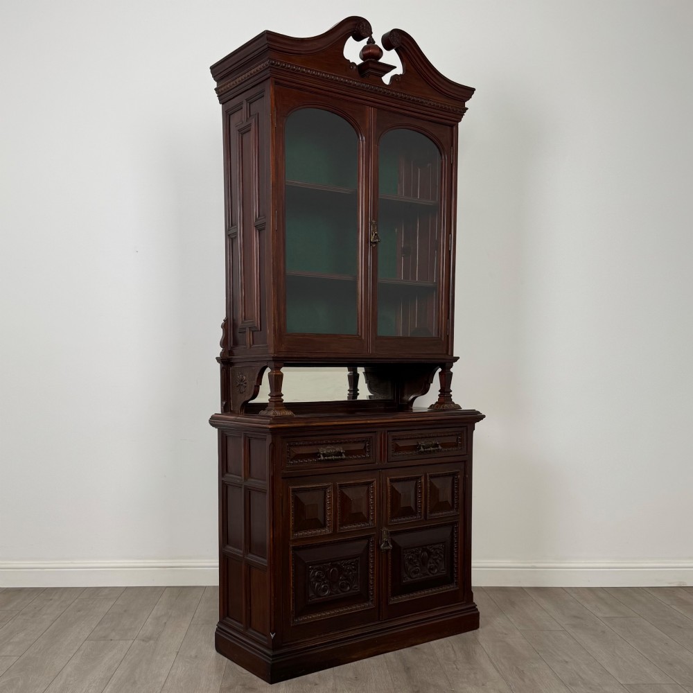 A nineteenth-century dark mahogany glazed bookcase featuring a carved swan neck pediment, twin arched glass upper doors, and a lower two-door cabinet with carved panels. View IX