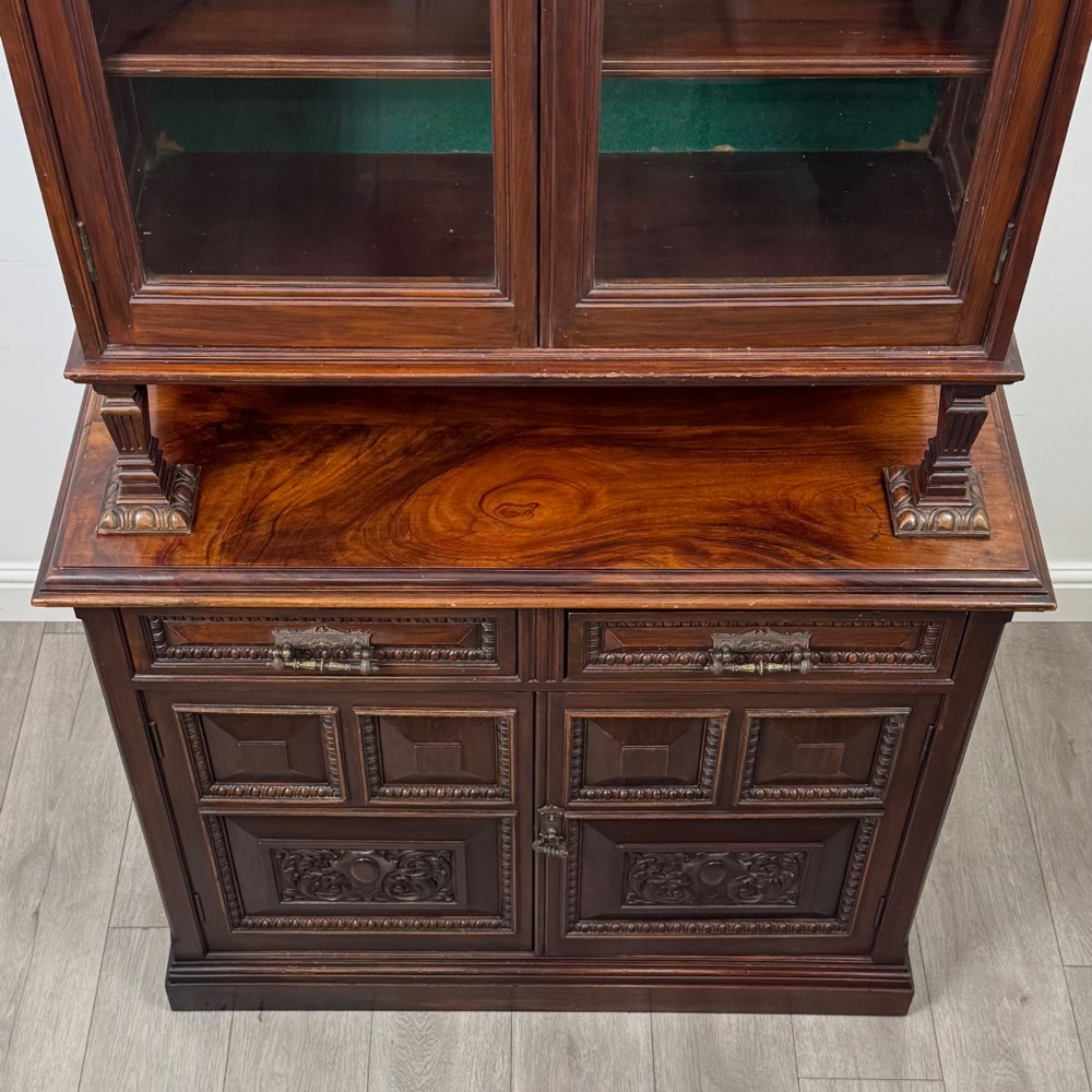 A nineteenth-century dark mahogany glazed bookcase featuring a carved swan neck pediment, twin arched glass upper doors, and a lower two-door cabinet with carved panels. View X