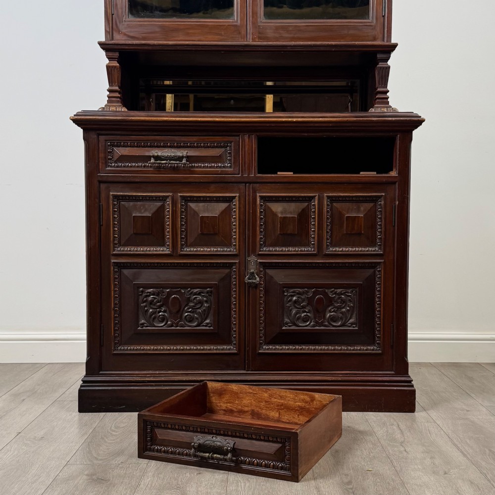 A nineteenth-century dark mahogany glazed bookcase featuring a carved swan neck pediment, twin arched glass upper doors, and a lower two-door cabinet with carved panels. View XI