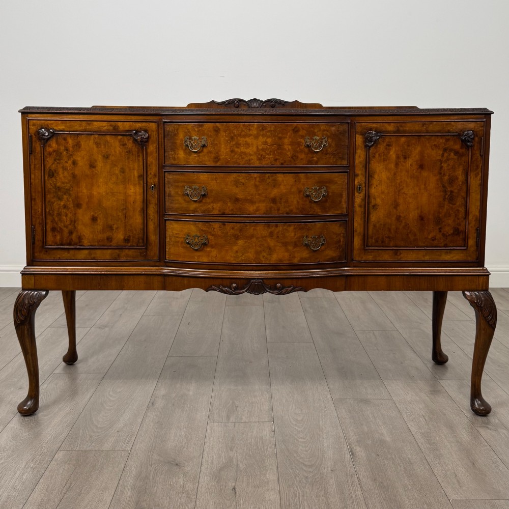 A 20th-century burr walnut sideboard featuring three central bowfront drawers flanked by cupboard doors, supported on carved cabriole legs.