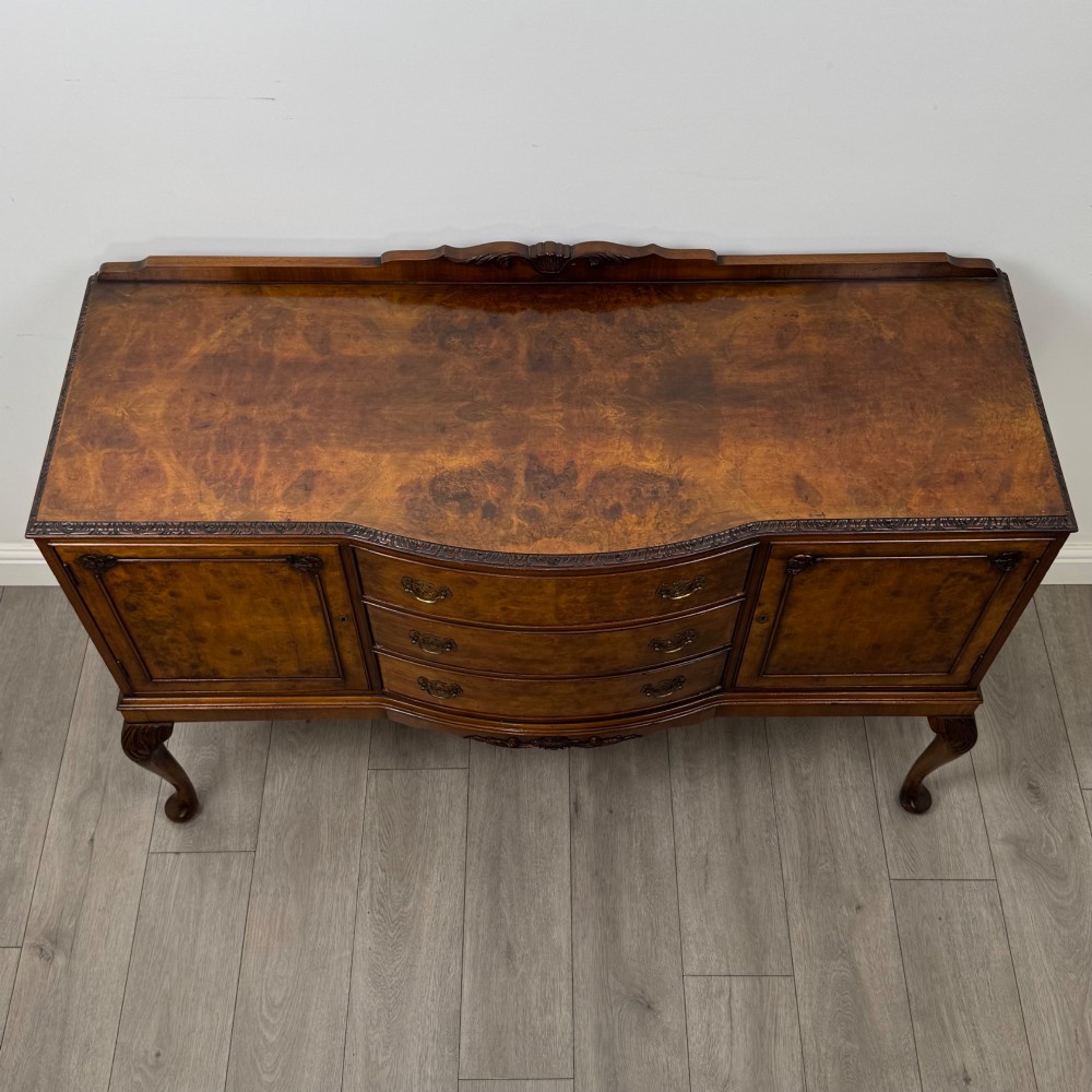 A 20th-century burr walnut sideboard featuring three central bowfront drawers flanked by cupboard doors, supported on carved cabriole legs. View X