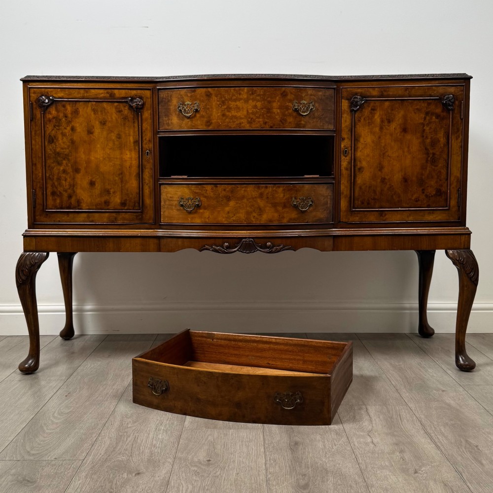 A 20th-century burr walnut sideboard featuring three central bowfront drawers flanked by cupboard doors, supported on carved cabriole legs. View XI