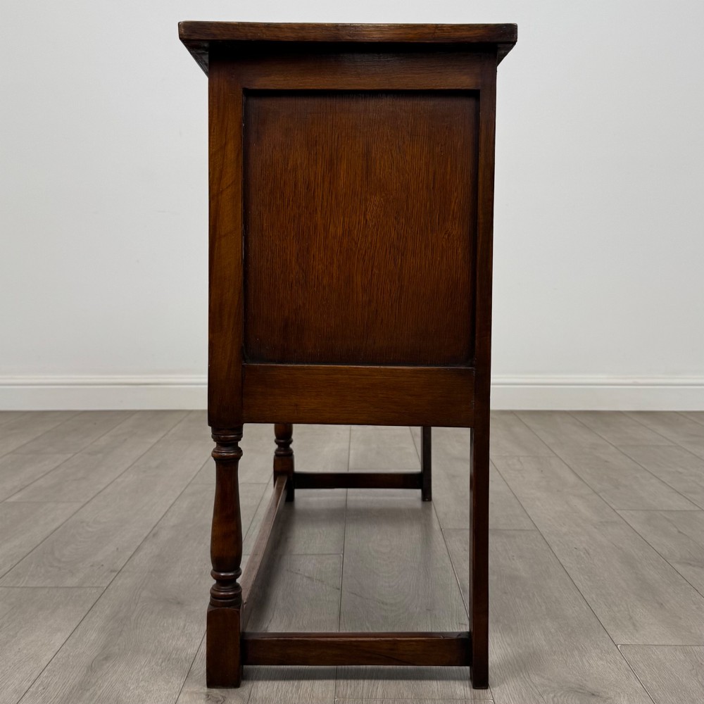 A dark oak cupboard featuring two door panels with carved Gothic arch motifs, wooden turn latches, and turned front legs connected by a perimeter stretcher. View IV