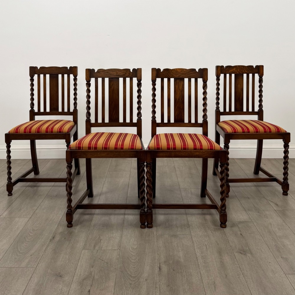 A set of four dark oak dining chairs featuring slatted backrests, barley twist front legs, and red and gold striped upholstered seat pads.