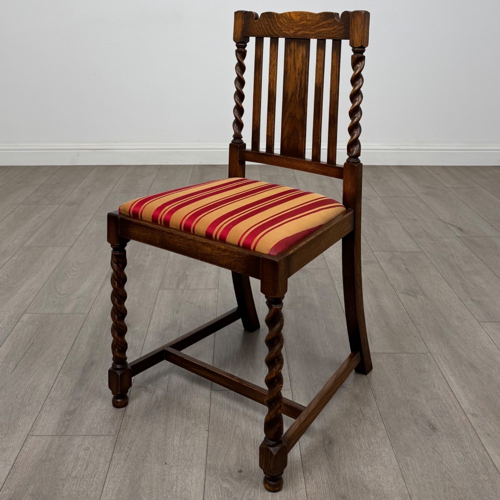 A set of four dark oak dining chairs featuring slatted backrests, barley twist front legs, and red and gold striped upholstered seat pads. View II