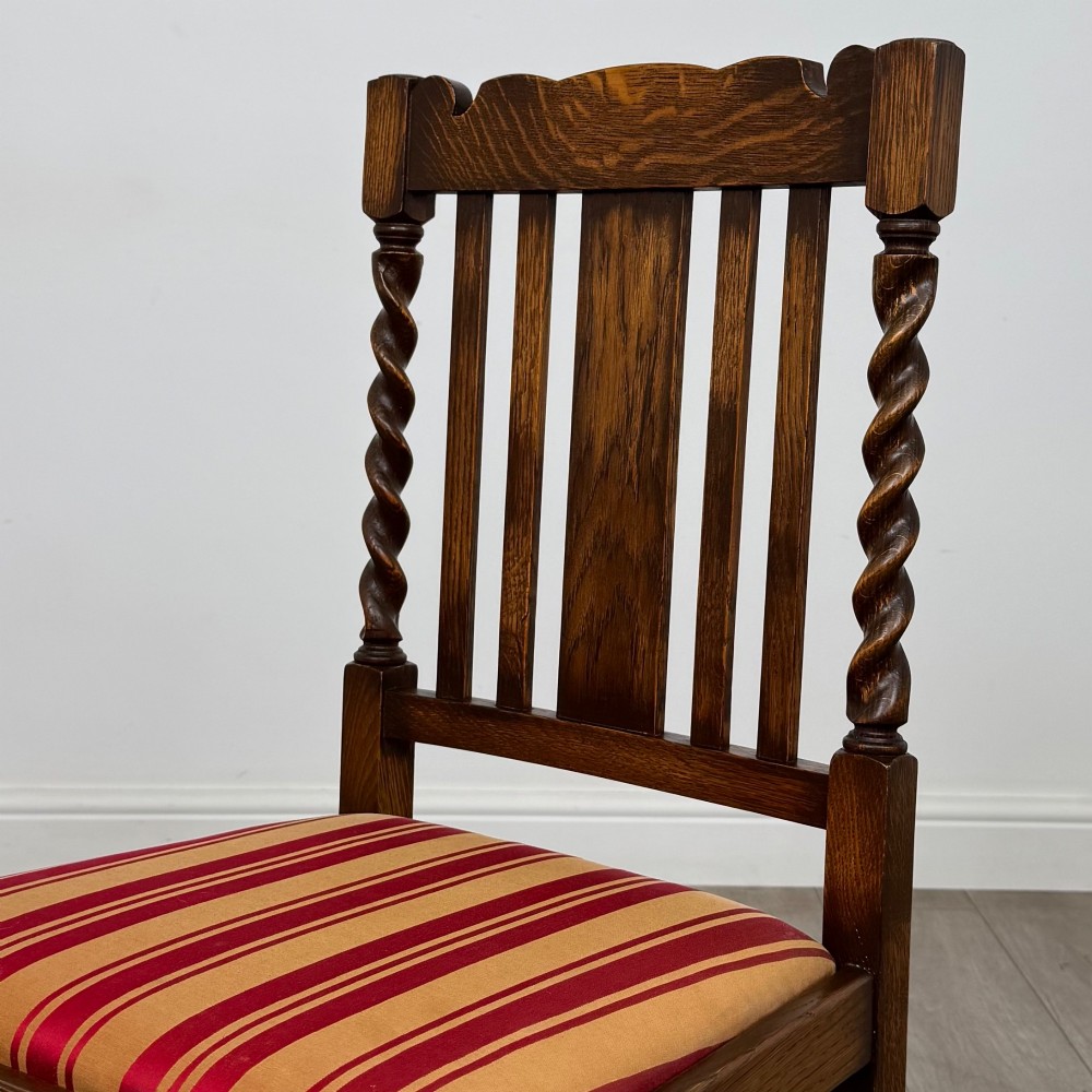 A set of four dark oak dining chairs featuring slatted backrests, barley twist front legs, and red and gold striped upholstered seat pads. View IV