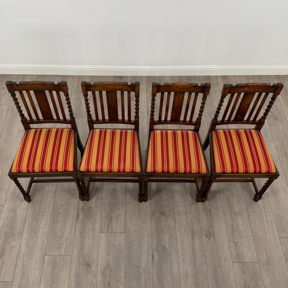 A set of four dark oak dining chairs featuring slatted backrests, barley twist front legs, and red and gold striped upholstered seat pads. View VII
