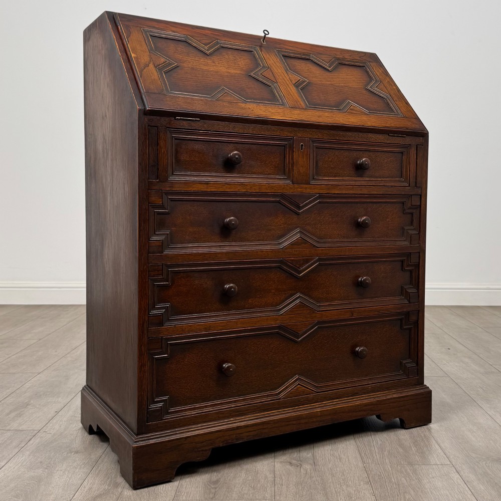 A dark oak Jacobean style slant-front bureau featuring geometric inlaid panels and four drawer fronts with turned wooden knobs. View IX