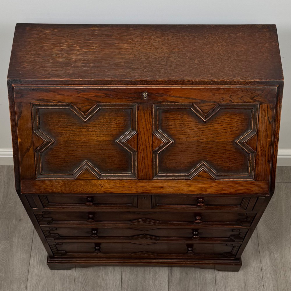 A dark oak Jacobean style slant-front bureau featuring geometric inlaid panels and four drawer fronts with turned wooden knobs. View X