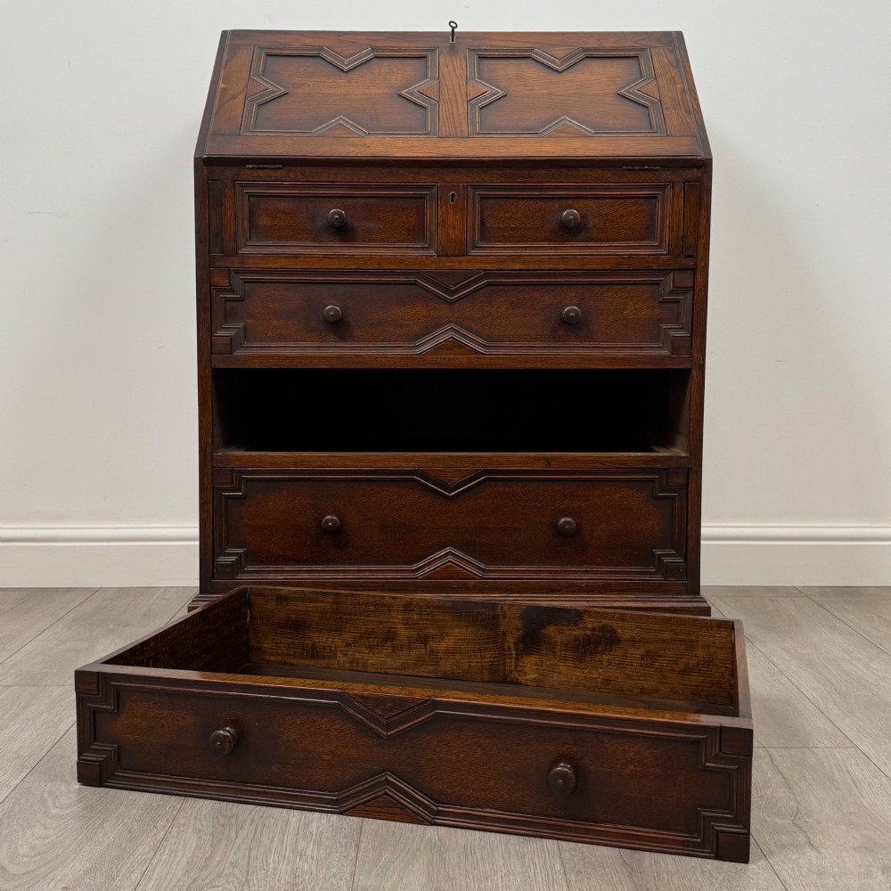 A dark oak Jacobean style slant-front bureau featuring geometric inlaid panels and four drawer fronts with turned wooden knobs. View XII