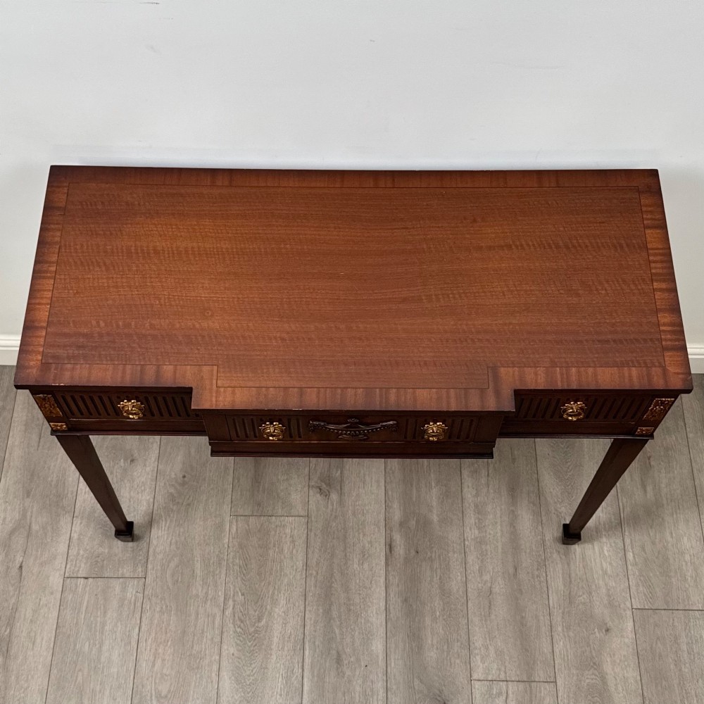 A dark mahogany 20th-century Adam style side table featuring a central carved urn motif, fluted frieze drawers, brass ring handles, and square tapered legs ending in spade feet. View IX