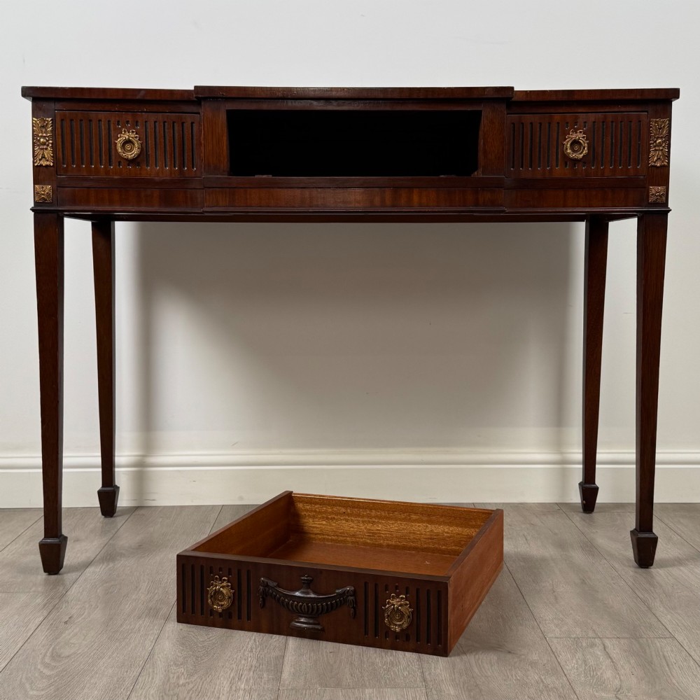A dark mahogany 20th-century Adam style side table featuring a central carved urn motif, fluted frieze drawers, brass ring handles, and square tapered legs ending in spade feet. View X