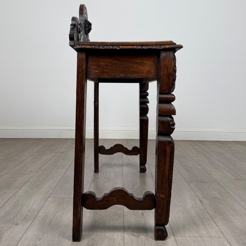 A dark carved oak Victorian side table featuring a sculpted mask upstand gallery, relief-carved frieze, and detailed carved legs. View VII