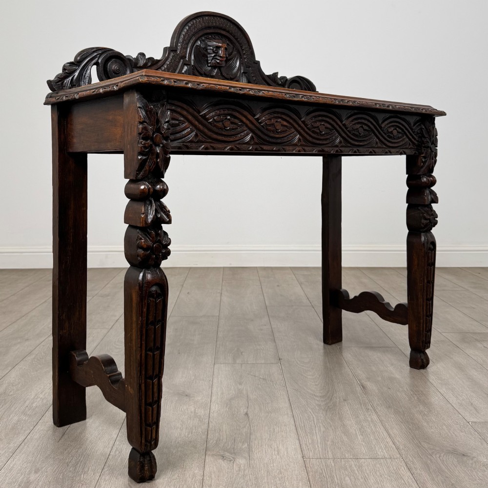 A dark carved oak Victorian side table featuring a sculpted mask upstand gallery, relief-carved frieze, and detailed carved legs. View VIII