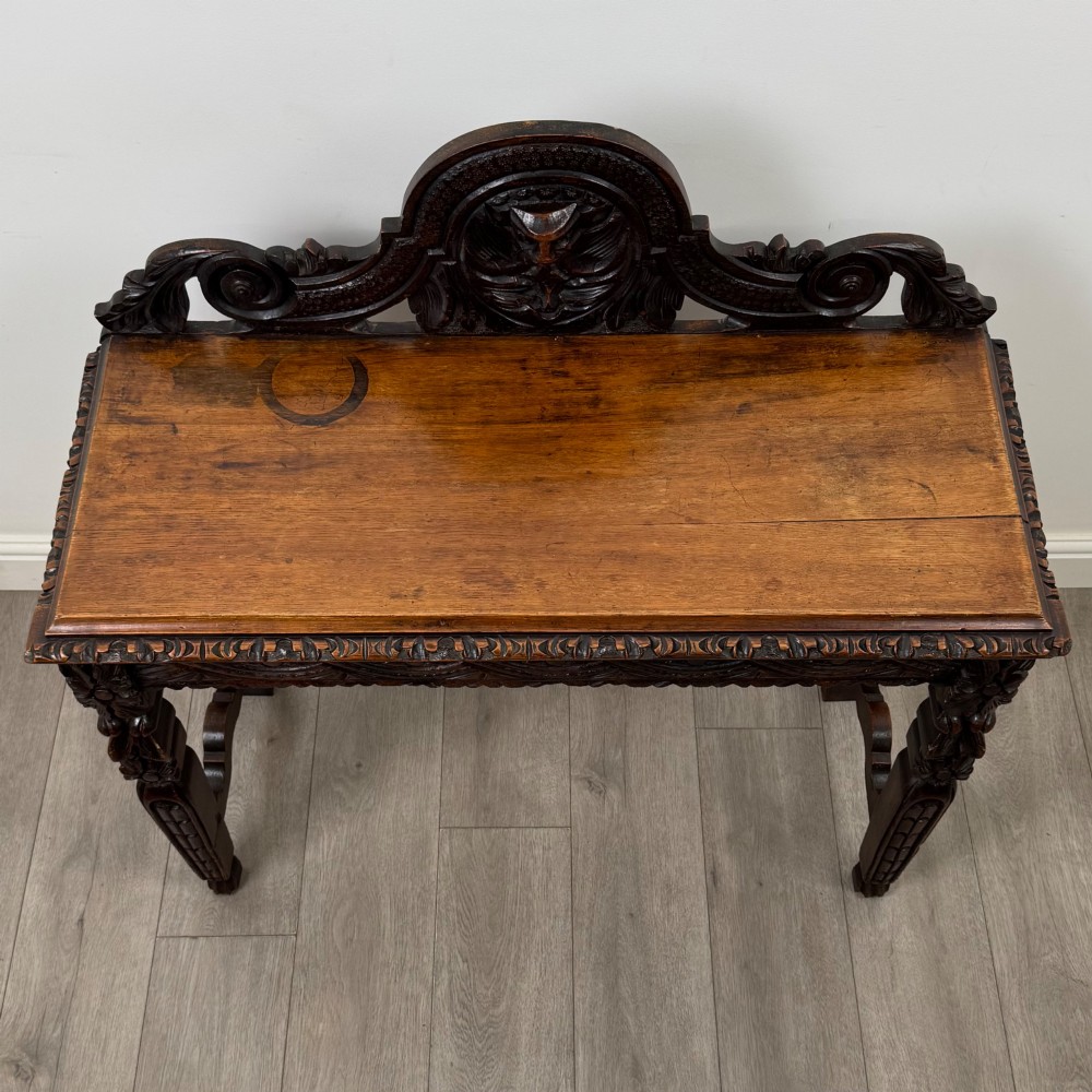 A dark carved oak Victorian side table featuring a sculpted mask upstand gallery, relief-carved frieze, and detailed carved legs. View IX