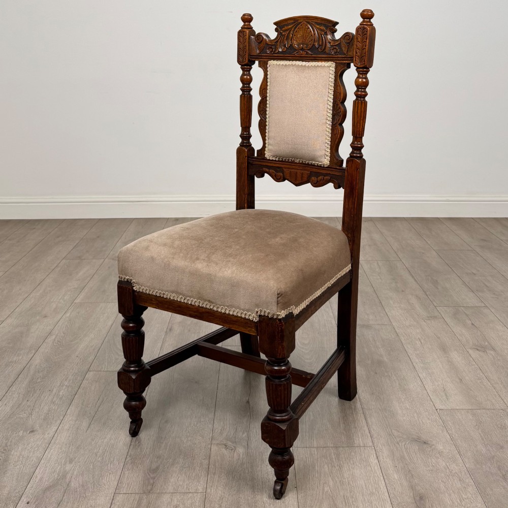 A set of four 19th-century Victorian carved oak dining chairs featuring beige upholstered seats, turned legs, and detailed crest carved backrests. View II