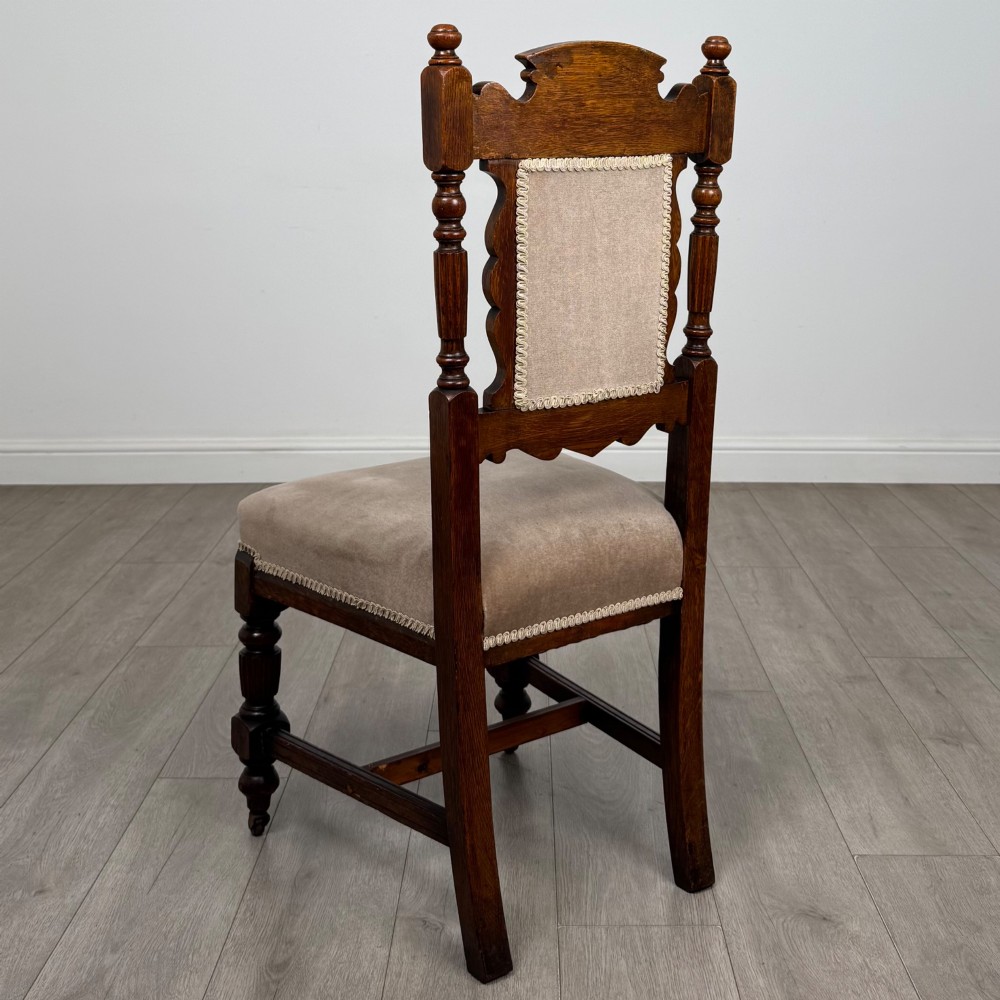 A set of four 19th-century Victorian carved oak dining chairs featuring beige upholstered seats, turned legs, and detailed crest carved backrests. View III