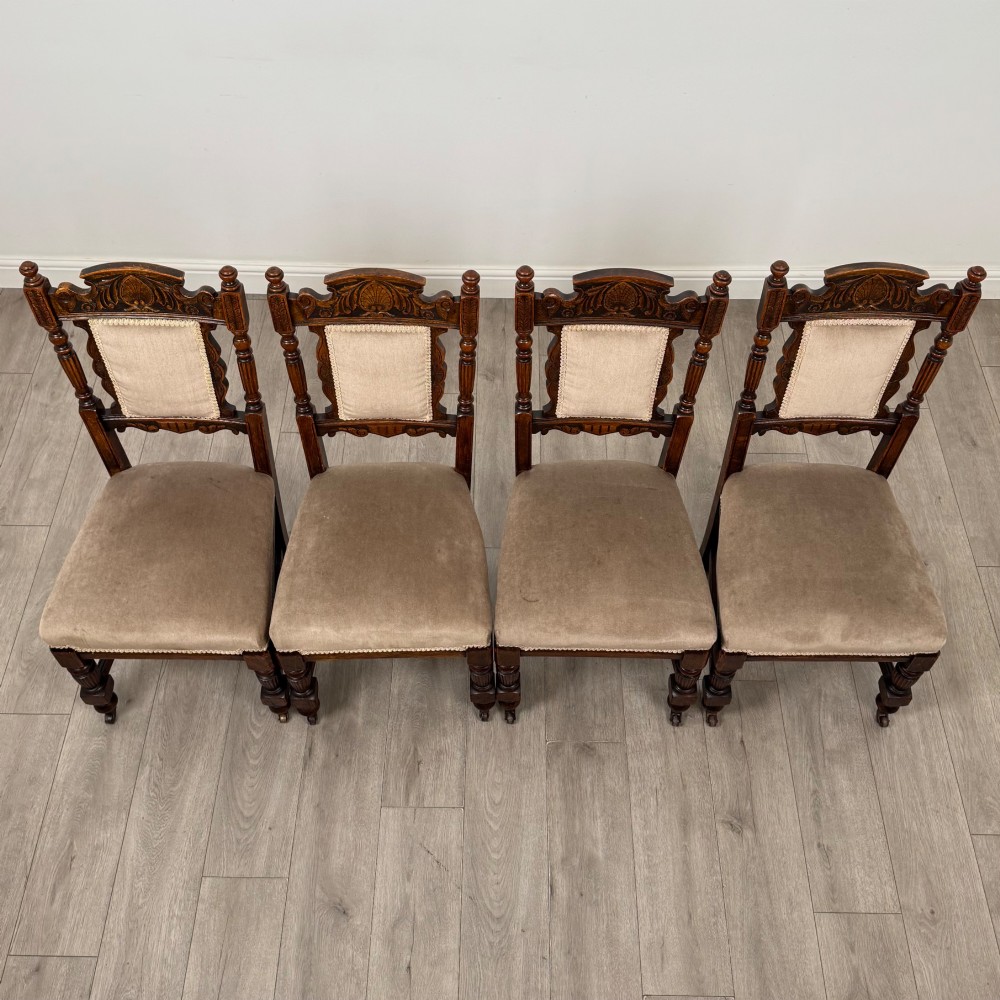 A set of four 19th-century Victorian carved oak dining chairs featuring beige upholstered seats, turned legs, and detailed crest carved backrests. View VII