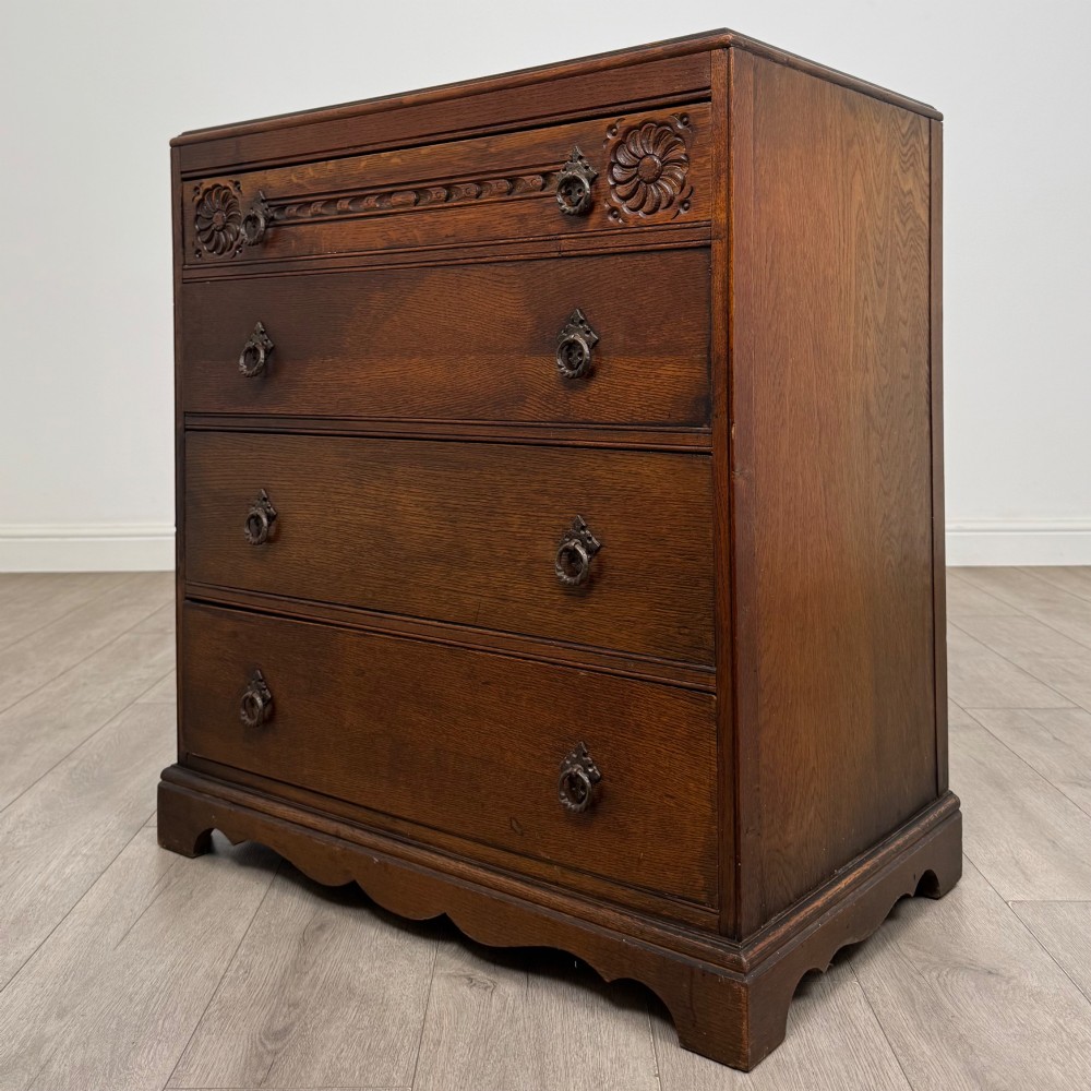A dark oak chest of four drawers decorated with carved floral rosettes and dark metal drop ring handles. View II