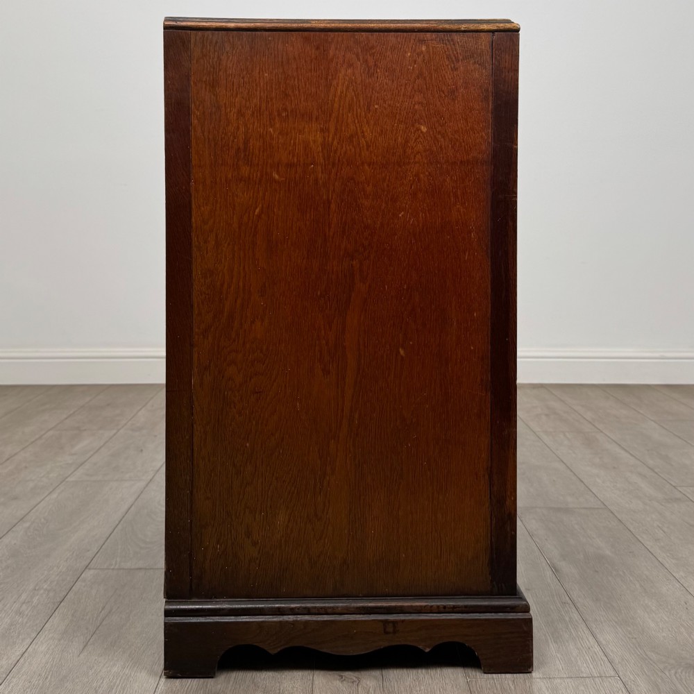 A dark oak chest of four drawers decorated with carved floral rosettes and dark metal drop ring handles. View VII