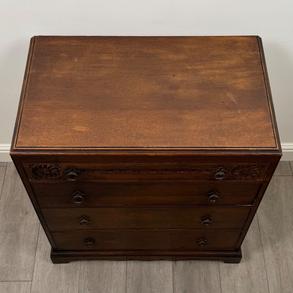 A dark oak chest of four drawers decorated with carved floral rosettes and dark metal drop ring handles. View IX