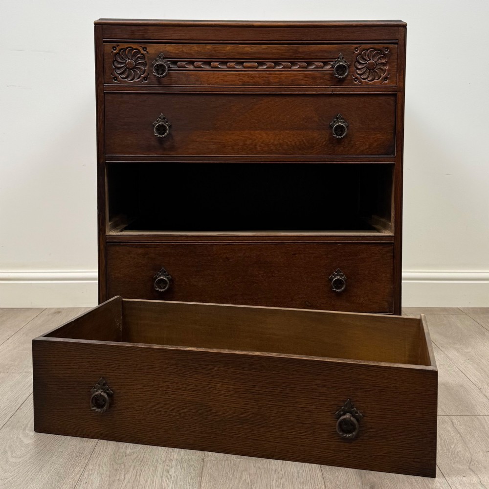 A dark oak chest of four drawers decorated with carved floral rosettes and dark metal drop ring handles. View X