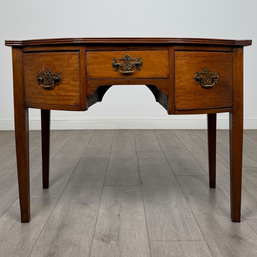 An 18th-century Georgian mahogany writing table with a bow-front top, three drawers fitted with brass handles, supported by square tapered legs.