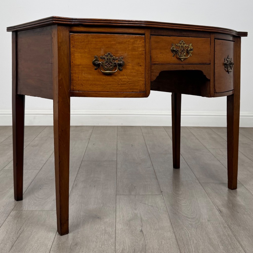 An 18th-century Georgian mahogany writing table with a bow-front top, three drawers fitted with brass handles, supported by square tapered legs. View VIII