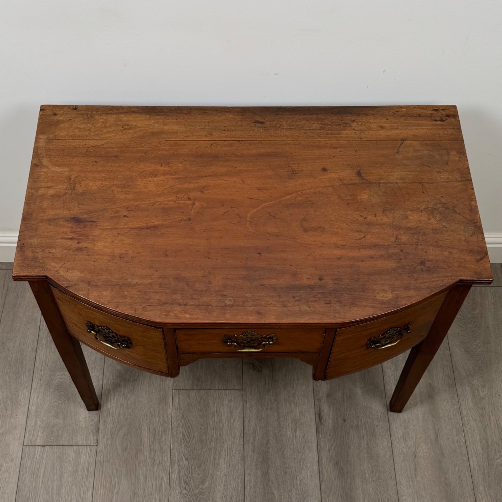 An 18th-century Georgian mahogany writing table with a bow-front top, three drawers fitted with brass handles, supported by square tapered legs. View IX