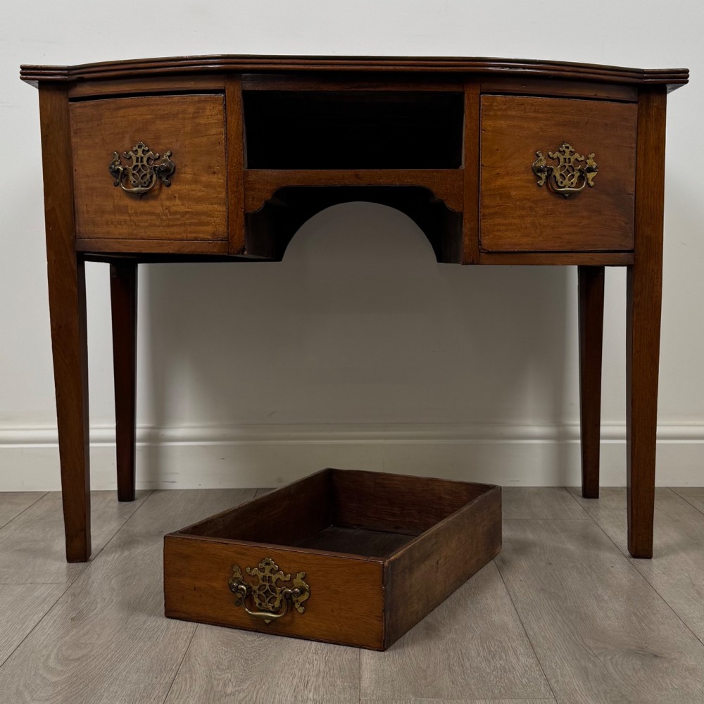 An 18th-century Georgian mahogany writing table with a bow-front top, three drawers fitted with brass handles, supported by square tapered legs. View X