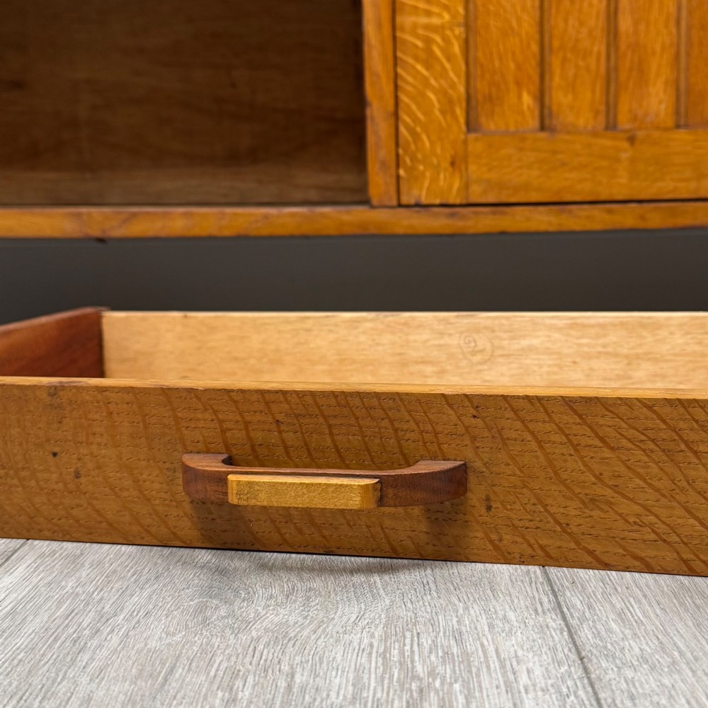 A compact golden oak sideboard featuring four shallow drawers on the left, an open shelf below, and a slatted single door cabinet on the right. View XII