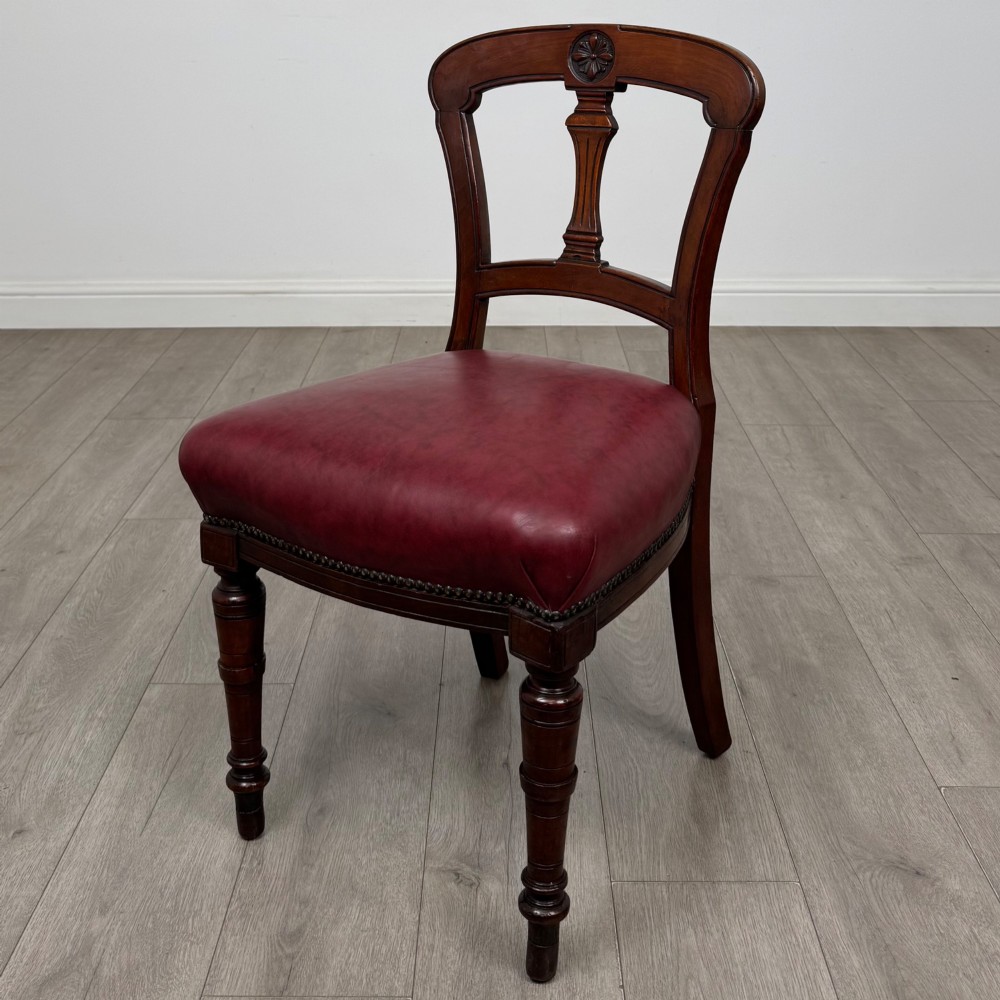 A set of four 19th-century mahogany dining chairs featuring carved open backs, dark red leather upholstered seats with stud trim, and turned front legs. View II