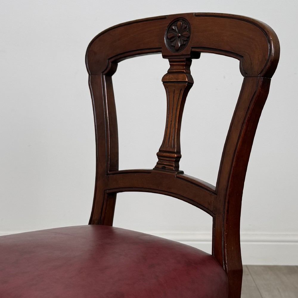 A set of four 19th-century mahogany dining chairs featuring carved open backs, dark red leather upholstered seats with stud trim, and turned front legs. View IV
