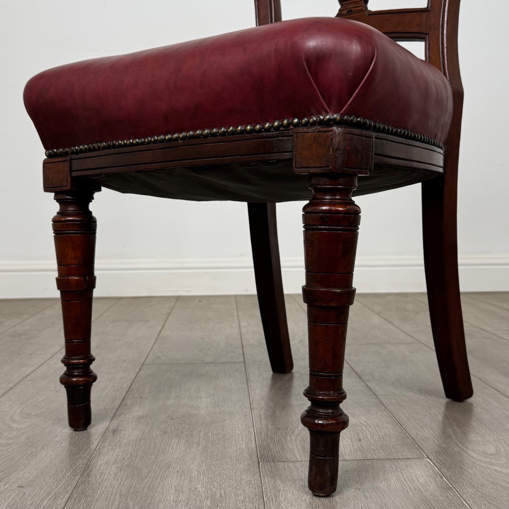 A set of four 19th-century mahogany dining chairs featuring carved open backs, dark red leather upholstered seats with stud trim, and turned front legs. View V