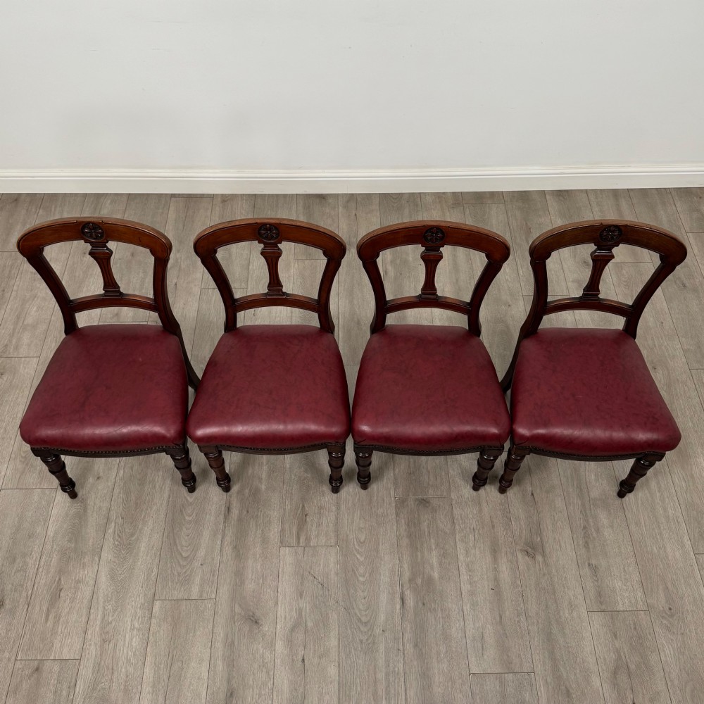 A set of four 19th-century mahogany dining chairs featuring carved open backs, dark red leather upholstered seats with stud trim, and turned front legs. View VII