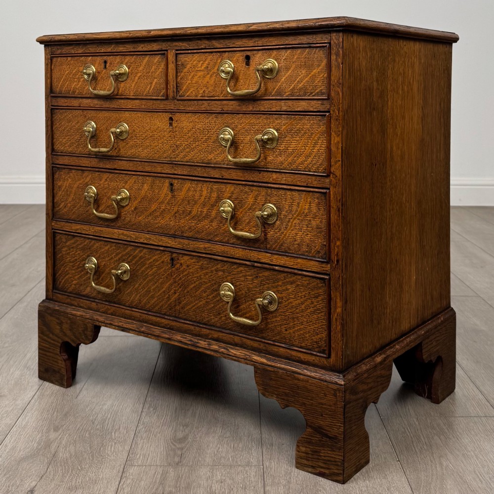 An antique oak chest of drawers featuring two short over three long drawers with brass swan-neck handles and shaped bracket feet. View II