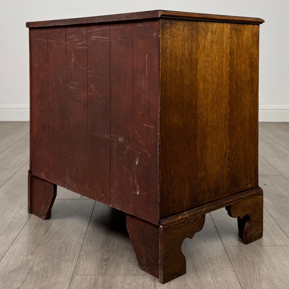 An antique oak chest of drawers featuring two short over three long drawers with brass swan-neck handles and shaped bracket feet. View VI