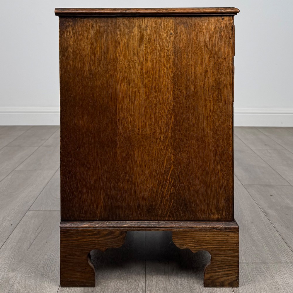 An antique oak chest of drawers featuring two short over three long drawers with brass swan-neck handles and shaped bracket feet. View VII