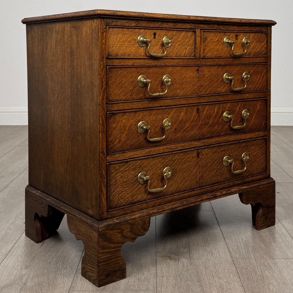 An antique oak chest of drawers featuring two short over three long drawers with brass swan-neck handles and shaped bracket feet. View VIII